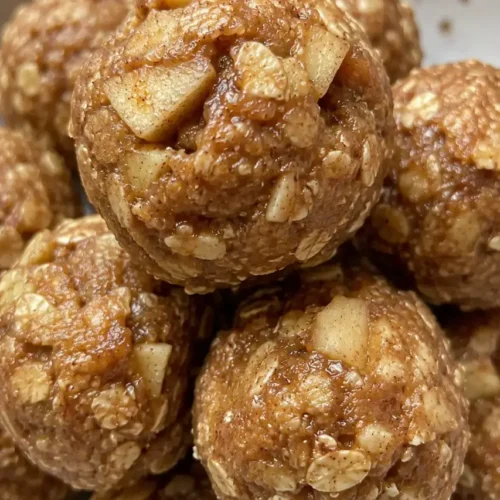 Apple cinnamon no bake energy bites in a bowl, surrounded by cinnamon sticks and dried apple pieces.