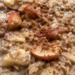 A bowl of no bake oatmeal topped with sliced apple and a cinnamon stick, drizzled with honey.