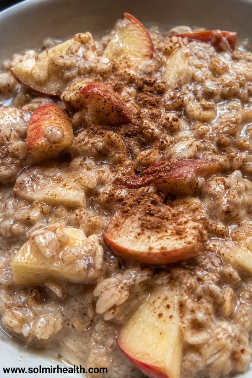 A bowl of no bake oatmeal topped with sliced apple and a cinnamon stick, drizzled with honey.