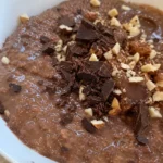 A bowl of dark chocolate-colored oatmeal with a spoon resting in it.