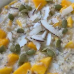 A jar of coconut oats topped with diced mango and shredded coconut.