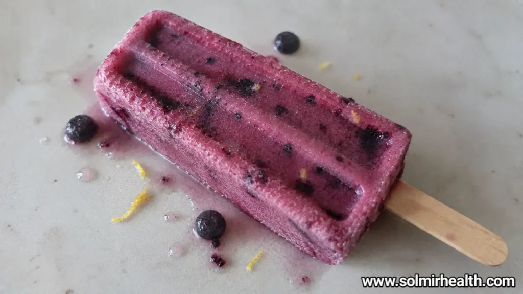 Blueberry lemon protein popsicles with a purple hue, topped with lemon zest.