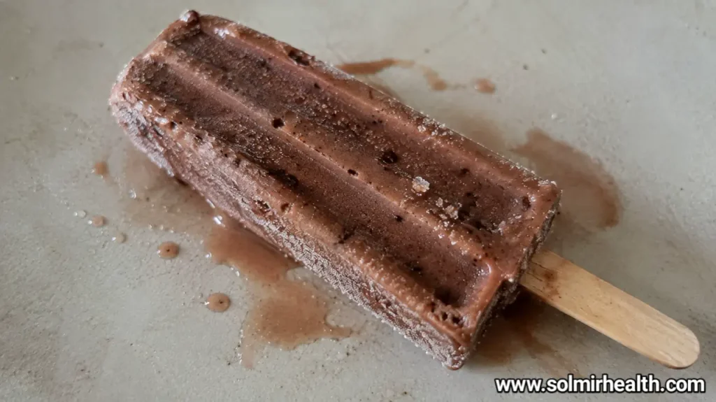 Chocolate protein popsicles with a smooth, fudgy texture next to sliced banana.