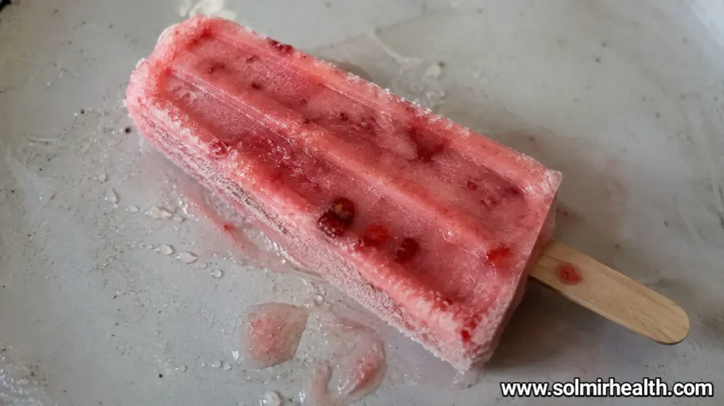Strawberry high protein popsicles with visible strawberry flecks, resting on a marble surface.